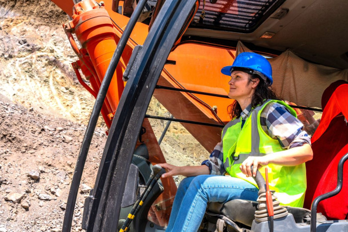 A woman wearing jeans, a high viz jacket and a hard hat operates a digger